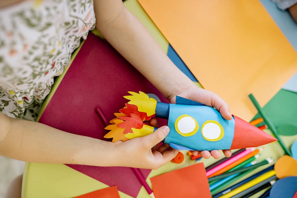 A child builds a vibrant paper rocket during an arts and crafts session, fostering creativity.